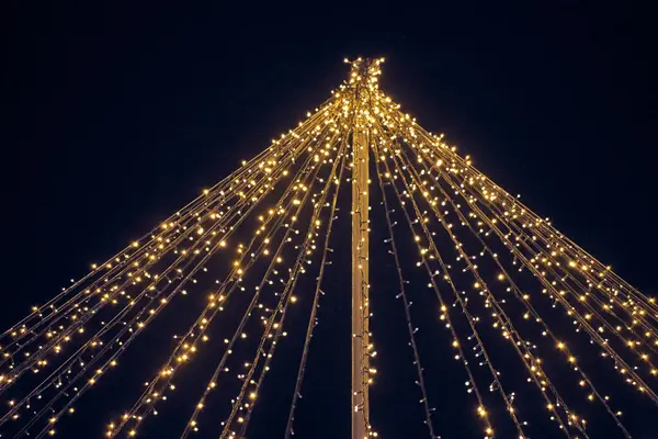 Sarı ışık çelenkleri gece mavi gökyüzü arka planında sütunlardan sarkan teller, sihirli tatil atmosferi. Parlak sarı ışıklı Noel çelenkleri, güzel açık hava dekorasyonu.