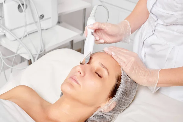 Cosmetologist makes facial ultrasonic peeling for rejuvenation woman face skincare, anti aging cosmetic procedure in beauty spa salon. Beautician makes face skin treatment with ultrasound scrubber