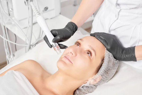 Beautician makes aqua exfoliation for rejuvenation woman face skincare, anti aging cosmetic procedure in beauty spa salon. Cosmetologist hands in black gloves makes face skin treatment for tightening