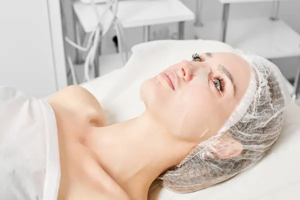 Young woman in sheet mask on face for rehydrate face skin, anti wrinkles cosmetic procedure in beauty spa salon. Beautiful female in moisturizing sheet mask in cosmetologist clinic, skin rejuvenation