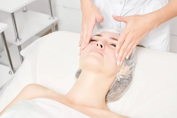 Cosmetologist massages woman face skin for rejuvenation, anti aging skincare cosmetic procedure in beauty spa salon. Beautician making facial massage with circular movements for beautiful female face