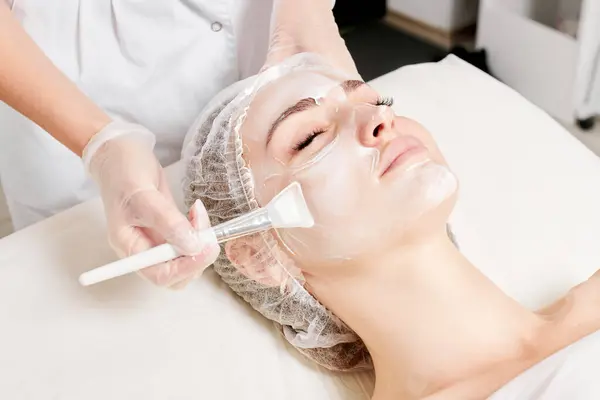 Kosmetolog Applicerar Kräm Mask Kvinnans Ansikte För Föryngring Ansikte Hud Stockbild