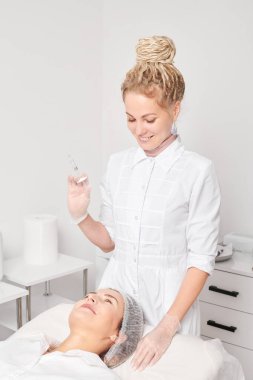 Şırıngalı kozmetik uzmanı kadının yüzüne gençleştirme iğnesi yapmaya hazırlanıyor. Güzellik salonunda yaşlanma karşıtı estetik ameliyat. Güzellik uzmanı yüz asidi enjeksiyonu tedavisi yapıyor.