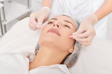 Kozmetik uzmanı güzellik salonundaki gençleştirme, yaşlanmayı önleyici kozmetik prosedürler için kadın yüzüne yüz yağı kapsülleri uyguluyor. Eldivenli güzellik uzmanı beslenme için yağ kapsülleri tutuyor.