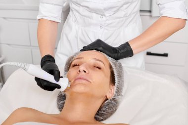 Güzellik uzmanı, güzellik salonundaki yaşlanma önleyici kozmetik işlemleri ve fonoforezi kullanarak gençleşen kadın yüzü için ultrason cildi sıkılaştırıyor. Kozmetik uzmanı ultrasonik deri kaldırıyor.