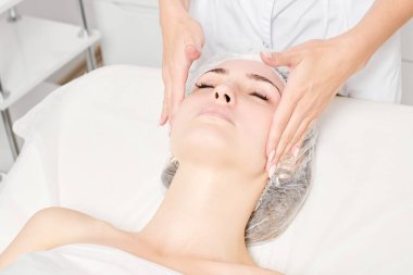 Güzellik uzmanları, güzellik salonlarında cilt bakımı, yaşlanma karşıtı estetik ameliyatlar için cilde masaj yapıyor. Kozmetik uzmanı güzel kadın yüzü için dairesel hareketlerle yüz masajı yapıyor.