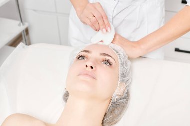 Gua Sha Taşı ile yüz masajı yapan kozmetik uzmanı, güzellik salonundaki lenfatik drenaj, yaşlanmayı önleyen estetik ameliyat için cilde bakıyor. Gua Sha aracıyla yüz masajı