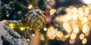 Sarı çelenkli Noel ağacı soğanları, karla kaplı açık hava ksenleri, dekoratif koni lambalı yeşil ağaç, açık hava kış tatili atmosferi. Süslemeleri ve çelenkleri olan Noel ağacı