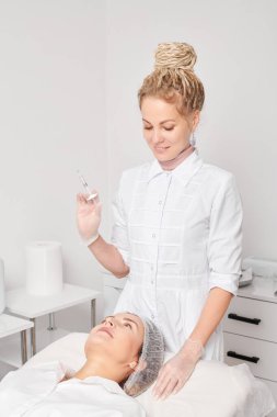 Şırıngalı kozmetik uzmanı kadının yüzüne gençleştirme iğnesi yapmaya hazırlanıyor. Güzellik salonunda yaşlanma karşıtı estetik ameliyat. Güzellik uzmanı yüz asidi enjeksiyonu tedavisi yapıyor.