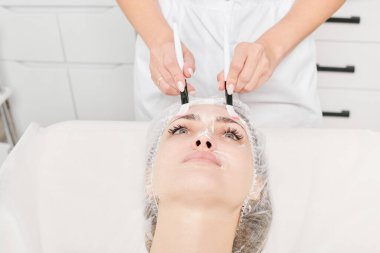 Güzellik uzmanı güzellik salonundaki cilt bakım kremi ve nemlendirici cilt bakımı için kadın derisine sürtünüyor. Kozmetik uzmanı elleri kadın yüzüne yüz kremi sürüyor.