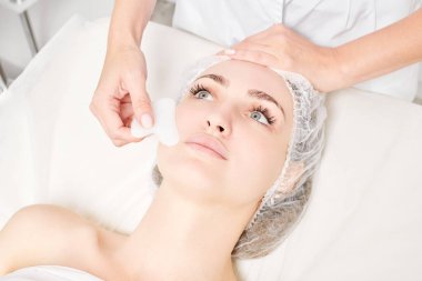 Gua Sha Taşı ile yüz masajı yapan kozmetik uzmanı, güzellik salonundaki lenfatik drenaj, yaşlanmayı önleyen estetik ameliyat için cilde bakıyor. Gua Sha aracıyla yüz masajı