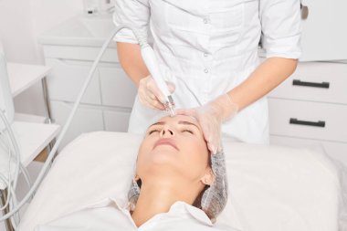 Güzellik uzmanı, güzellik salonundaki yaşlanma karşıtı kozmetik prosedürü olan cilt bakımını yenilemek için su bitkisi üretiyor. Eldivenleri teslim eden kozmetolog, sıkılaştırmak için yüz bakımı yapıyor