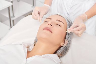 Kozmetik uzmanı güzellik salonundaki gençleştirme, yaşlanmayı önleyici kozmetik prosedürler için kadın yüzüne yüz yağı kapsülleri uyguluyor. Eldivenli güzellik uzmanı beslenme için yağ kapsülleri tutuyor.