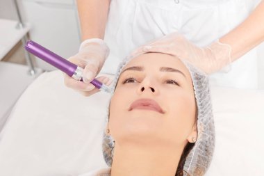 Kozmetik uzmanı, yenilenen kadın yüzü için mezoterapi enjeksiyonu yapıyor. Güzellik salonunda yaşlanmayı önleyen estetik cerrahi müdahale yok. Eldivenli güzellik uzmanı yüz mikro iğnesi yapar.