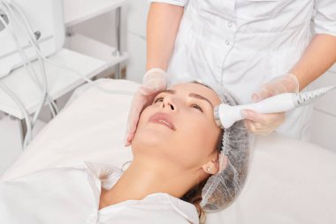 Kozmetik uzmanı, güzellik salonundaki yaşlanmayı önleyen kozmetik prosedürleri kullanarak gençleşen kadın yüzü için ultrason cildini sıkılaştırıyor. Güzellik uzmanı ultrasonik deri kaldırıyor.