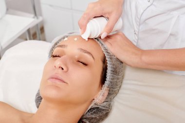 Güzellik uzmanı kadın yüzüne nemlendirici krem sürüyor cilt tazeleme, kaplıca salonunda rehidrasyon kozmetik prosedürü için. Profesyonel kozmetolog cilt bakımı için canlandırıcı krem maskesi uyguluyor.