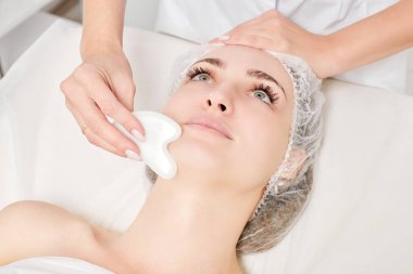 Güzellik uzmanı Gua Sha taşıyla yüz masajı yaparak güzellik salonundaki lenfatik drenaj, yaşlanmayı önleyen estetik ameliyatlar için cilde bakıyor. Gua Sha aracıyla yüz masajı