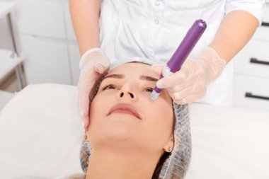 Güzellik uzmanı, gençleşen kadın yüzü için mezoterapi enjeksiyonu yapıyor. Güzellik salonunda yaşlanmayı önleyen estetik cerrahi prosedür uyguluyor. Eldivenleri teslim eden kozmetolog yüz mikro iğnesi yapıyor.