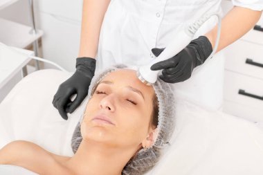 Kozmetik uzmanı, güzellik salonundaki yaşlanmayı önleyen kozmetik prosedürleri kullanarak gençleşen kadın yüzü için ultrason cildini sıkılaştırıyor. Güzellik uzmanı ultrasonik deri kaldırıyor.
