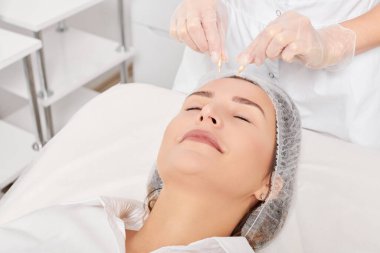 Güzellik uzmanı, güzellik salonundaki yaşlanma karşıtı kozmetik prosedürleri gençleştirme için kadın yüzüne yüz yağı kapsülleri uyguluyor. Eldivenleri teslim eden kozmetolojist beslenme için yağ kapsüllerini tutuyor.