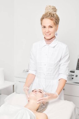 Güzellik uzmanı, güzellik salonundaki yaşlanma karşıtı kozmetik işlemler için kadın yüzüne krem maskesi takıyor. Kozmetik uzmanı kadın yüzüne krem sürerken eldiven verdi.