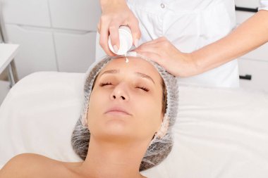 Kozmetik uzmanı kadın yüzüne nemlendirici krem sürüyor yüz yenileme için, kaplıca salonundaki rehidrasyon kozmetik prosedürü için. Profesyonel güzellik uzmanı cilt bakımı için canlandırıcı krem maske uyguluyor.
