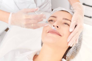 Kozmetik uzmanı güzellik salonunda dudak büyütme ve hacim için estetik cerrahi olmayan ameliyatlar yapıyor. Eldivenli güzellik uzmanı dudaklarına şırınga yapıyor.