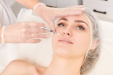 Kozmetik uzmanı güzellik salonunda dudak büyütme ve hacim için estetik cerrahi olmayan ameliyatlar yapıyor. Eldiven uzmanları şırınga ile iğne yapıyor.