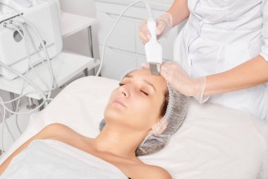 Kozmetik uzmanı, güzellik salonundaki yaşlanma karşıtı kozmetik prosedürleri, cilt bakımını yenilemek için yüz ultrasoniği yapıyor. Güzellik uzmanı yüz bakımını ultrason fırçasıyla yapıyor.
