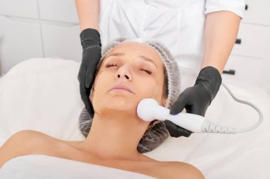 Güzellik uzmanı, güzellik salonundaki gençleştirme kadın yüzü için RF kaldırma, yaşlanma karşıtı kozmetik işlemleri yapıyor. Kozmetik uzmanı, kadın yüz derisinde artan kolajen için radyo frekansı tedavisi yapıyor.