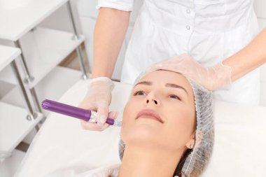 Güzellik uzmanı, gençleşen kadın yüzü için mezoterapi enjeksiyonu yapıyor. Güzellik salonunda yaşlanmayı önleyen estetik cerrahi prosedür uyguluyor. Eldivenleri teslim eden kozmetolog yüz mikro iğnesi yapıyor.