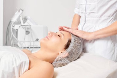 Güzellik uzmanları, güzellik salonlarında gençleştirme için nemlendirici krem maskeyi kadın yüzüne sürerler, yaşlanma karşıtı kozmetik işlemler yaparlar. Kozmetik uzmanı kadın derisi için yüz kremi uyguluyor.