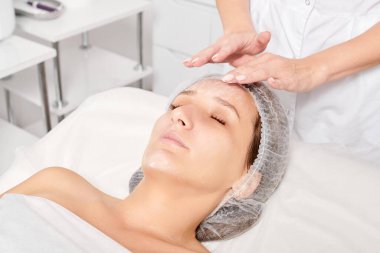 Güzellik uzmanları, güzellik salonlarında gençleştirme için nemlendirici krem maskeyi kadın yüzüne sürerler, yaşlanma karşıtı kozmetik işlemler yaparlar. Kozmetik uzmanı kadın derisi için yüz kremi uyguluyor.