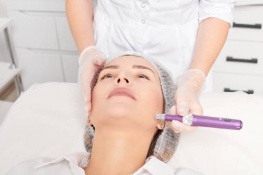 Güzellik uzmanı, gençleşen kadın yüzü için mezoterapi enjeksiyonu yapıyor. Güzellik salonunda yaşlanmayı önleyen estetik cerrahi prosedür uyguluyor. Eldivenleri teslim eden kozmetolog yüz mikro iğnesi yapıyor.