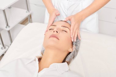 Kozmetik uzmanı, güzellik salonundaki gençleştirme için nemlendirici krem sürdükten sonra cildine masaj yapıyor. Güzellik uzmanları kadın yüzüne masaj yapar.
