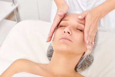 Kozmetik uzmanı, güzellik salonundaki cilt bakımı, yaşlanmayı önleyen estetik ameliyatlar için cilde masaj yapıyor. Güzellik uzmanı güzel kadın yüzü için dairesel hareketlerle yüz masajı yapıyor.