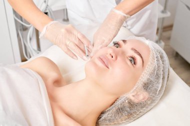 Kozmetik uzmanı kadın yüzüne gençleştirme enjeksiyonu yapıyor. Güzellik salonunda yaşlanmayı önleyen estetik cerrahi olmayan prosedür uyguluyor. Eldiven uzmanları şırınga ile iğne yapıyor.