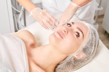 Kozmetik uzmanı kadın yüzüne gençleştirme enjeksiyonu yapıyor. Güzellik salonunda yaşlanmayı önleyen estetik cerrahi olmayan prosedür uyguluyor. Eldiven uzmanları şırınga ile iğne yapıyor.