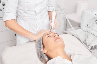 Güzellik uzmanı, güzellik salonundaki yaşlanma karşıtı kozmetik prosedürü olan cilt bakımını yenilemek için su bitkisi üretiyor. Eldivenleri teslim eden kozmetolog, sıkılaştırmak için yüz bakımı yapıyor