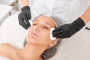 Kozmetikçiler güzellik salonundaki yüz kremi maskesini kadın yüzünden kozmetik mendillerle temizliyor, cilt yenileme estetik ameliyatları yapıyor. Güzellik uzmanları yüz maskesini çıkarmak için peçete tutuyor.