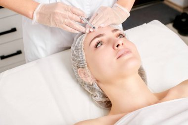 Kozmetik uzmanı kadın yüzüne gençleştirme enjeksiyonu yapıyor. Güzellik salonunda yaşlanmayı önleyen estetik cerrahi olmayan prosedür uyguluyor. Eldiven uzmanları şırınga ile iğne yapıyor.