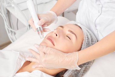 Güzellik uzmanı, güzellik salonundaki yaşlanma karşıtı kozmetik prosedürü olan cilt bakımını yenilemek için su bitkisi üretiyor. Eldivenleri teslim eden kozmetolog, sıkılaştırmak için yüz bakımı yapıyor