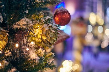 Sarı çelenklerle süslenmiş Noel ağacı süsleri karla kaplı, açık havada kırmızı soğanlı yeşil ağaç, açık havada kış tatili atmosferi. Süslemeleri ve çelenkleri olan Noel ağacı