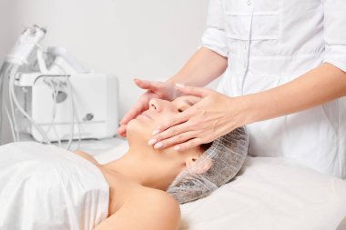 Güzellik uzmanları, güzellik salonlarında gençleştirme için nemlendirici krem maskeyi kadın yüzüne sürerler, yaşlanma karşıtı kozmetik işlemler yaparlar. Kozmetik uzmanı kadın derisi için yüz kremi uyguluyor.