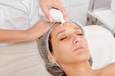 Kozmetik uzmanı kadın yüzüne nemlendirici krem sürüyor yüz yenileme için, kaplıca salonundaki rehidrasyon kozmetik prosedürü için. Profesyonel güzellik uzmanı cilt bakımı için canlandırıcı krem maske uyguluyor.