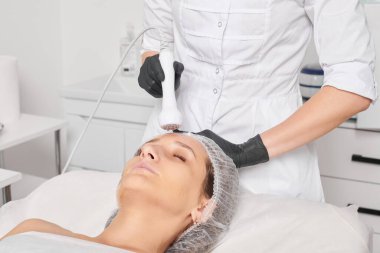 Güzellik uzmanı, güzellik salonundaki gençleştirme kadın yüzü için RF kaldırma, yaşlanma karşıtı kozmetik işlemleri yapıyor. Kozmetik uzmanı, kadın yüz derisinde artan kolajen için radyo frekansı tedavisi yapıyor.