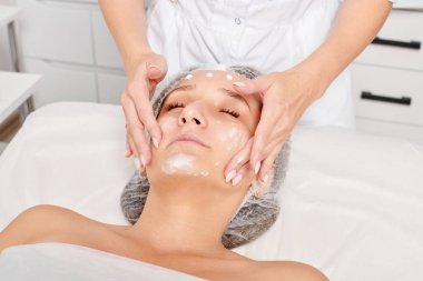 Güzellik uzmanları, güzellik salonlarında gençleştirme için nemlendirici krem maskeyi kadın yüzüne sürerler, yaşlanma karşıtı kozmetik işlemler yaparlar. Kozmetik uzmanı kadın derisi için yüz kremi uyguluyor.