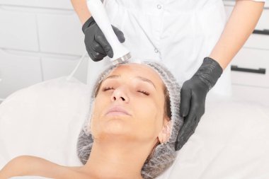 Güzellik uzmanı, güzellik salonundaki yaşlanma önleyici kozmetik işlemleri ve fonoforezi kullanarak gençleşen kadın yüzü için ultrason cildi sıkılaştırıyor. Kozmetik uzmanı ultrasonik deri kaldırıyor.