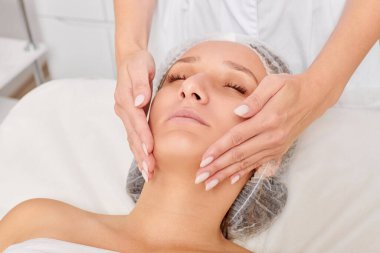 Güzellik uzmanları, güzellik salonlarında cilt bakımı, yaşlanma karşıtı estetik ameliyatlar için cilde masaj yapıyor. Güzel kadın yüzü için kozmetik kremiyle yüz masajı yapıyor.