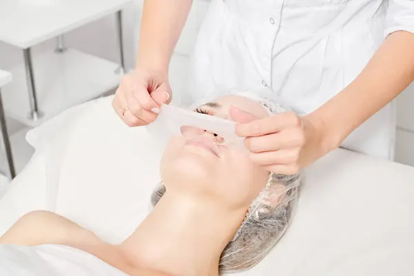 Beautician removing sheet mask on woman face for rehydrate face skin, anti aging cosmetic procedure in beauty spa salon. Cosmetologist removing moisturizing sheet mask on female face